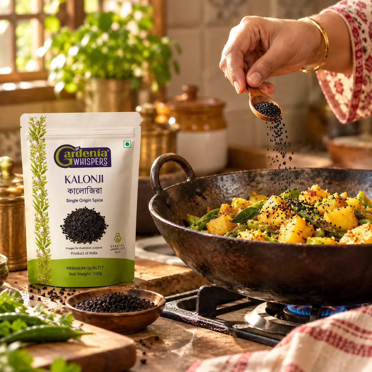 Gardenia Whispers Kalonji Nigella Seeds 100g pack being sprinkled from wooden spoon over aloo sabzi in iron kadai