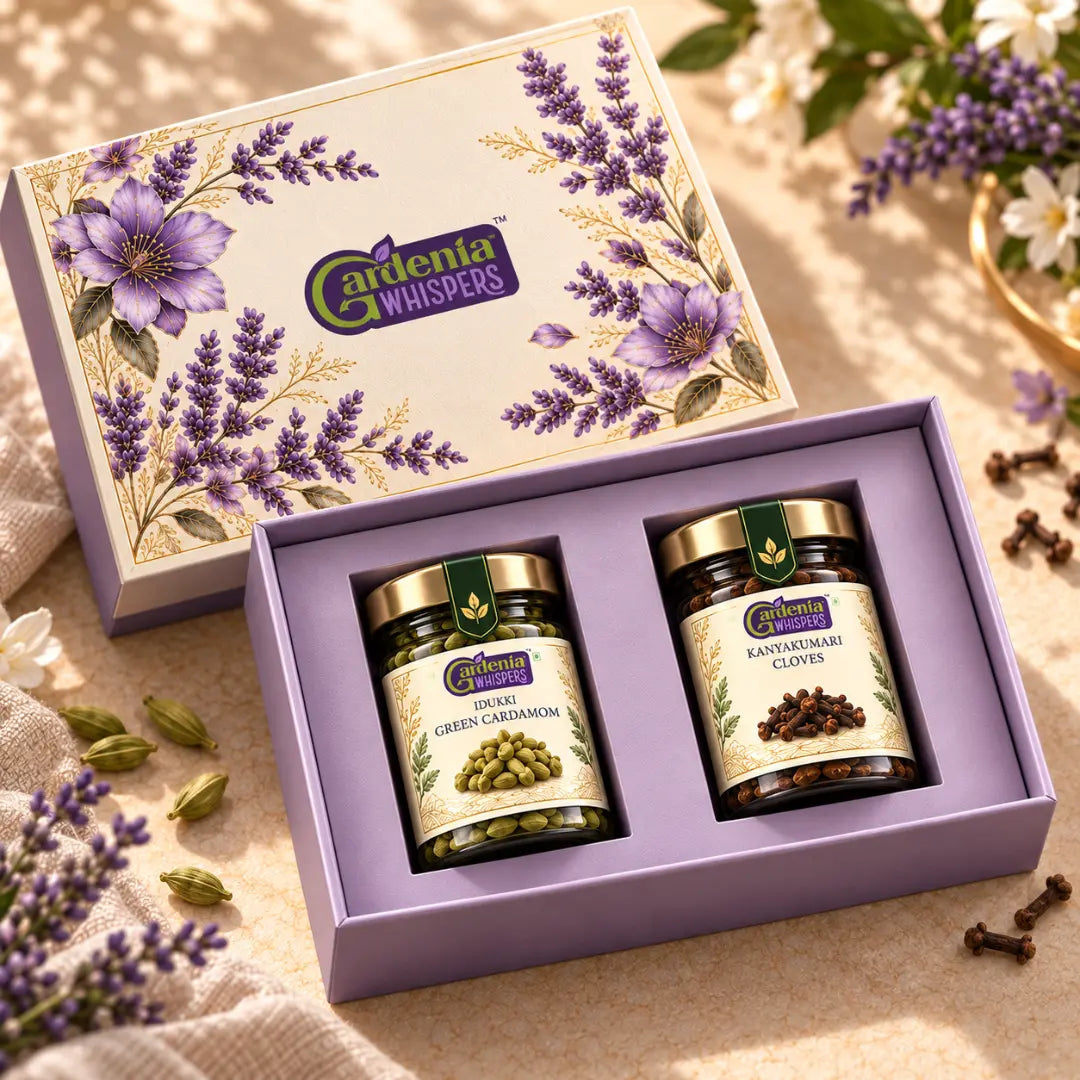 Gardenia Whispers Lavender gift box angled top view showing two spice jars inside purple box with lavender floral lid propped open, scattered cardamom pods, cloves and lavender sprigs on beige surface