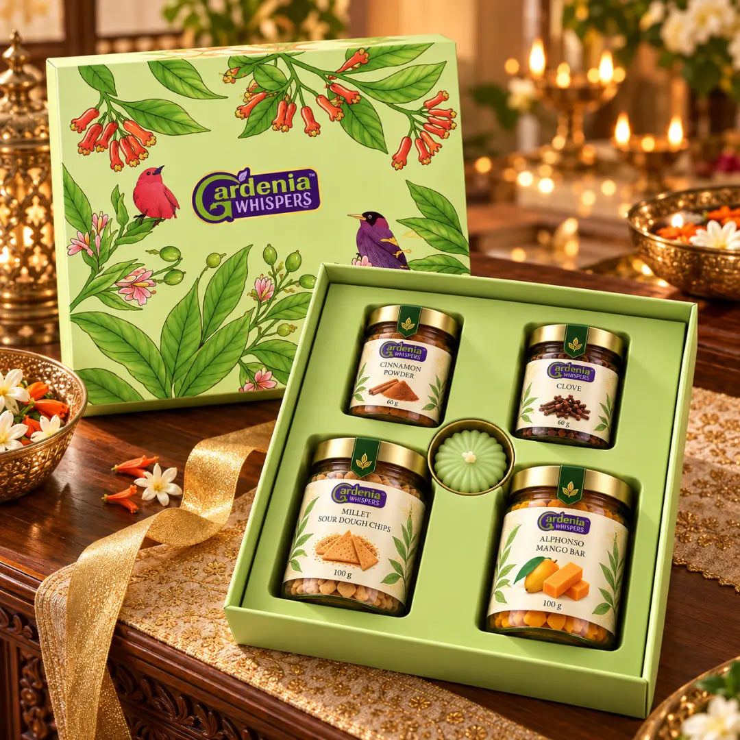 Gardenia Whispers Parijat festive gift box open front view with four spice and snack jars and green rosette centrepiece, surrounded by brass diyas, marigold petals and autumn leaves in a Diwali setting